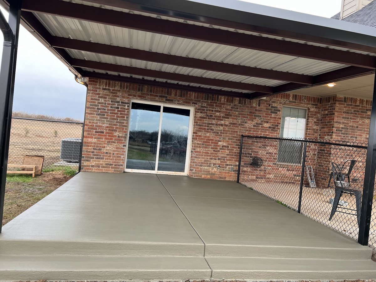 Freshly finished concrete patio and steps beneath a covered brick porch.