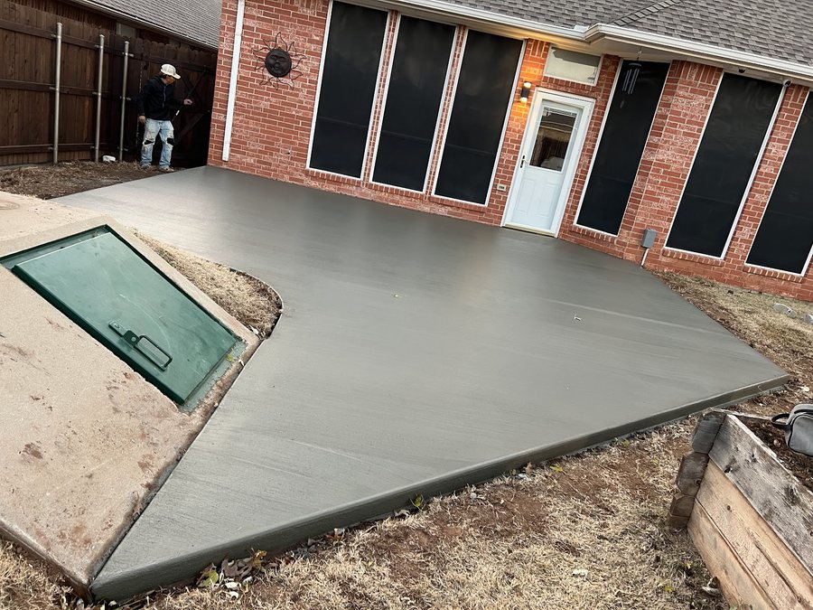 Covered brick porch with a broad finished concrete patio and two steps.