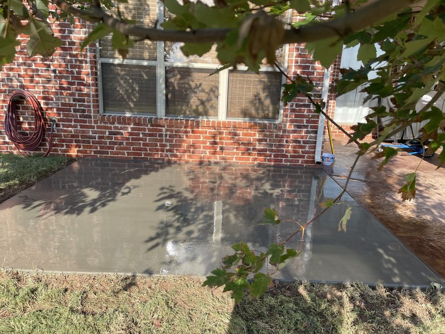 Broad finished concrete driveway and entry slab beside a brick home.