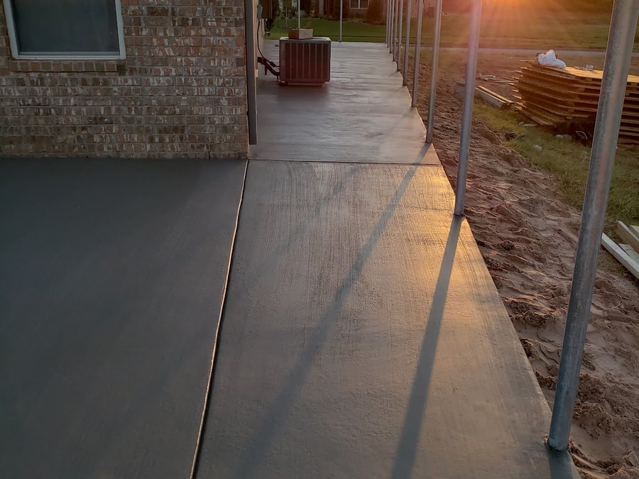 New concrete walkway and slab leading toward a house under construction.