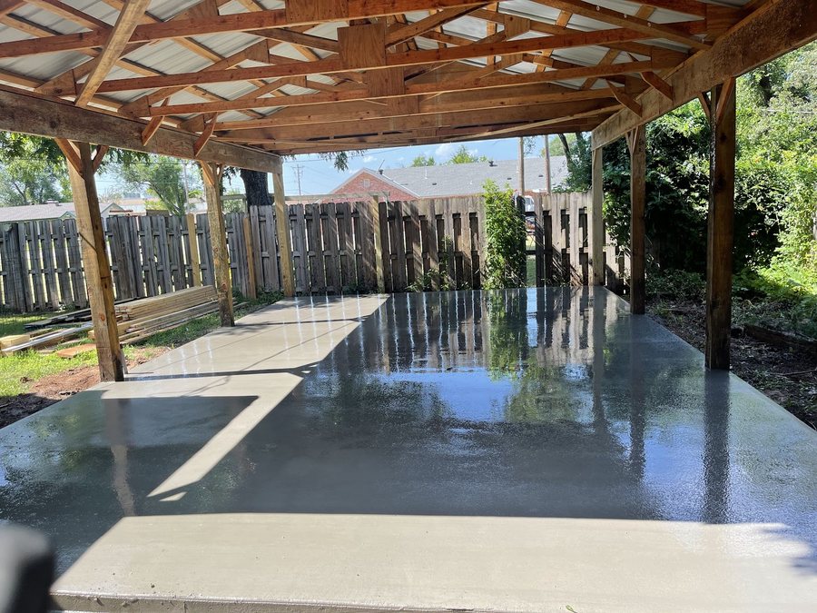 New rectangular backyard concrete pad beside an existing covered patio and lawn.